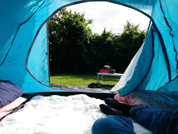 Sezione bassa di un uomo seduto in tenda contro il cielo blu