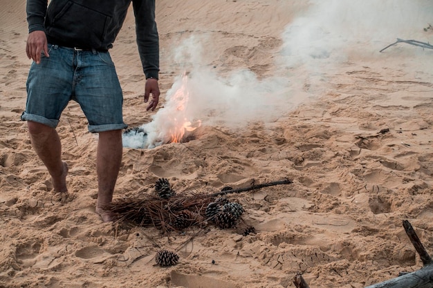 Sezione bassa di un uomo vicino a un falò sulla spiaggia sabbiosa