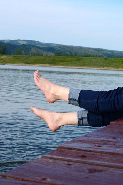 Sezione bassa di una donna con le gambe pendenti mentre è seduta sul molo sul lago