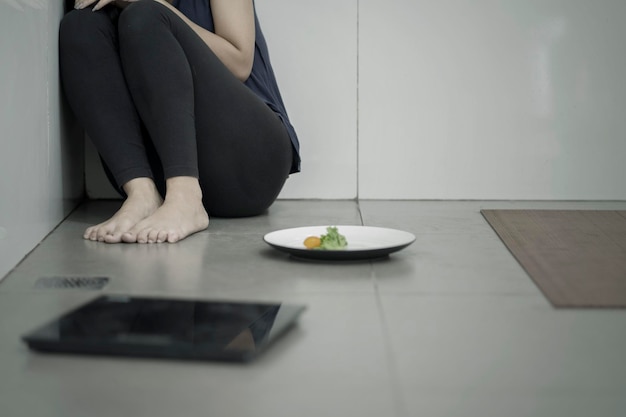 Sezione bassa di una donna seduta vicino al cibo in un piatto sul pavimento a casa