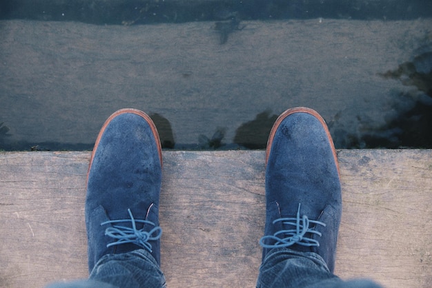 Sezione bassa di una persona in piedi su una tavola di legno vicino all'acqua