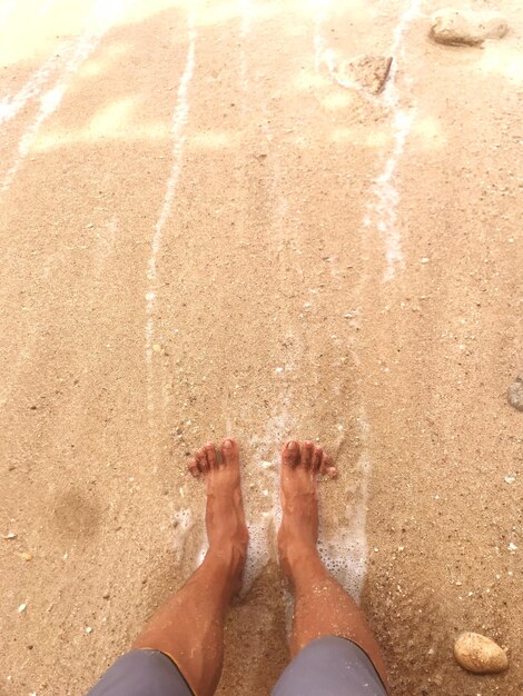 Sezione bassa di una persona in piedi sulla spiaggia sabbiosa