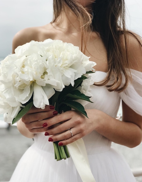Sezione centrale della sposa che tiene un bouquet bianco durante la cerimonia nuziale