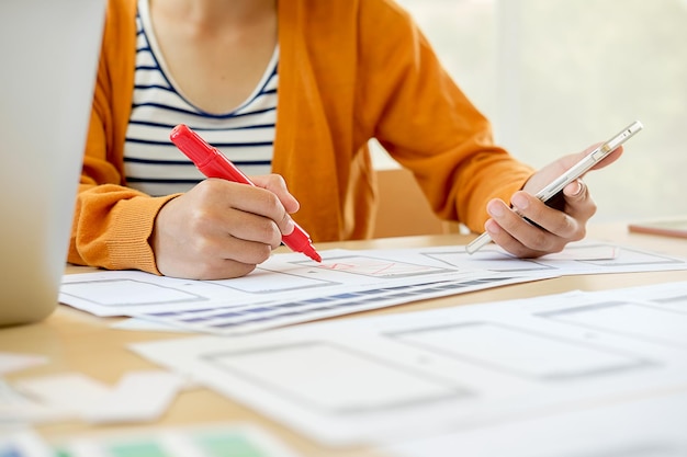 Sezione centrale di un'architetto donna che tiene in mano un telefono cellulare mentre disegna diagrammi al tavolo