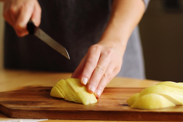 Sezione centrale di una donna che taglia patate su un tavolo da taglio in cucina