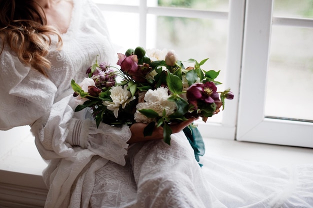 Sezione centrale di una donna che tiene dei fiori mentre è seduta sul davanzale della finestra