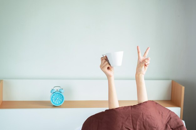 Sezione centrale di una donna con una tazza di caffè sul tavolo contro il muro a casa.