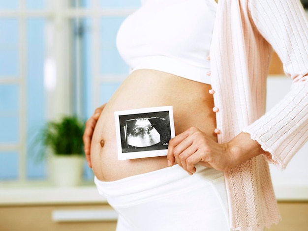 Sezione centrale di una donna incinta che tiene una fotografia mentre è in piedi all'interno