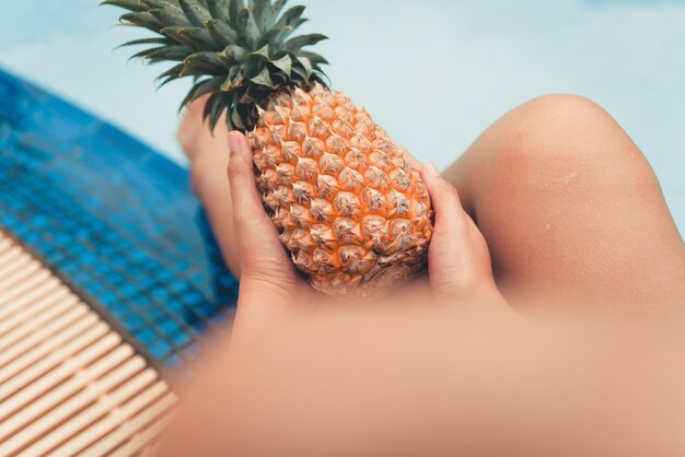 Sezione centrale di una persona che tiene un ananas mentre è seduta vicino alla piscina