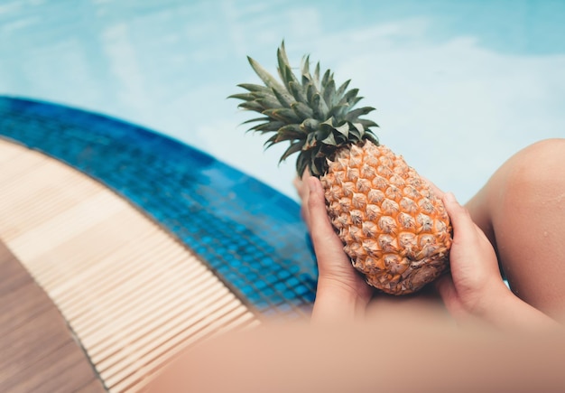 Sezione centrale di una persona che tiene un ananas mentre è seduta vicino alla piscina