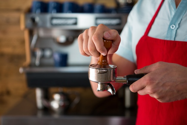 Sezione mediana del barista maschio che utilizza un tamper per premere il caffè macinato nel portafiltro nella caffetteria