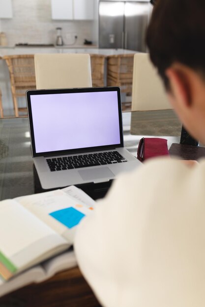 Sezione mediana dell'adolescente asiatico con libri e laptop sul tavolo che studia a casa, copia spazio