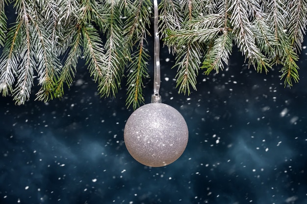 Sfera bianca di Natale su un albero di Natale durante una nevicata