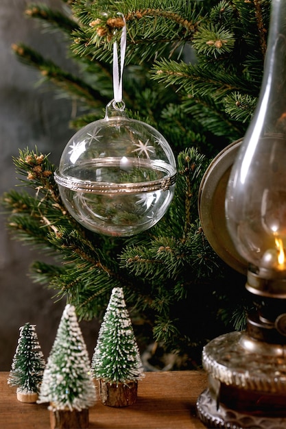 Sfera di apertura vuota in vetro trasparente per esposizione di prodotti o regali con lampada a cherosene vintage decorativa di alberi di Natale su tavolo di legno, abete sullo sfondo. Concetto di pubblicità per le vacanze di Capodanno