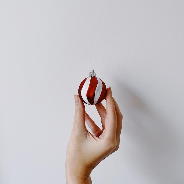 Sfera di pallina lucida in oro a mano femminile su sfondo bianco Decorazione estetica minimalista per le feste di Capodanno di Natale