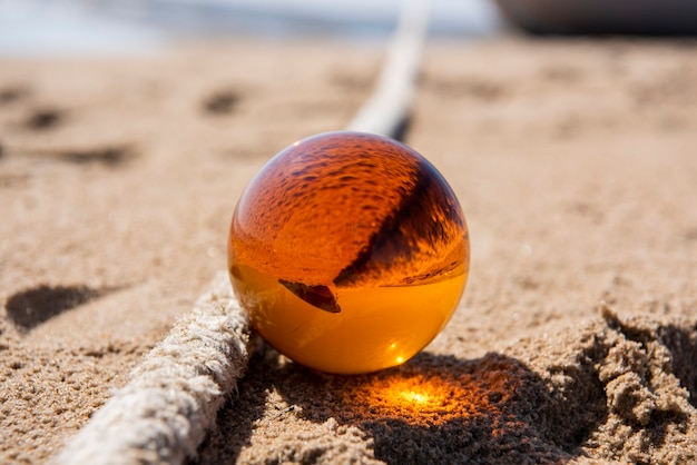 Sfera di vetro arancione sulla sabbia vicino al mare