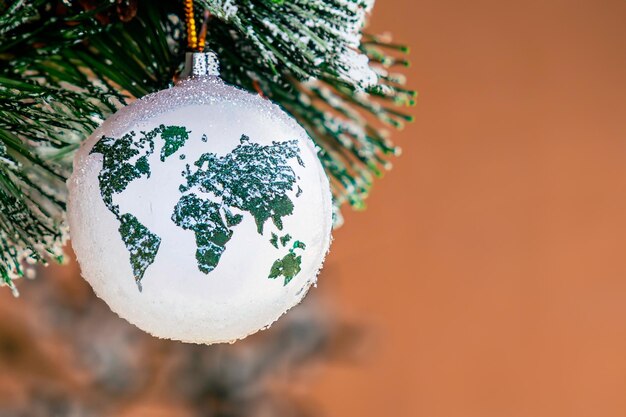 Sfera di vetro di Natale con una figura a forma di mappa del mondo appesa a un ramo di pino