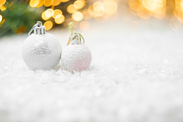 Sfere decorative di natale che risiedono in una neve con bokeh luci gialle