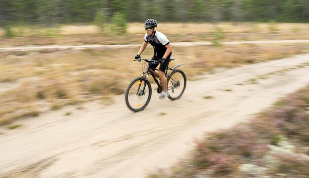 Sfocata nella foto in movimento un uomo veloce su una mountain bike con casco e marcia sulla strada nella foresta