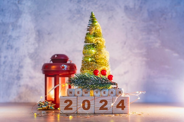 Sfondio delle vacanze di Capodanno con una lampada luminosa con candele accese Iscrizione su cubi di legno del numero 2024 con un albero di Natale e luci luminose