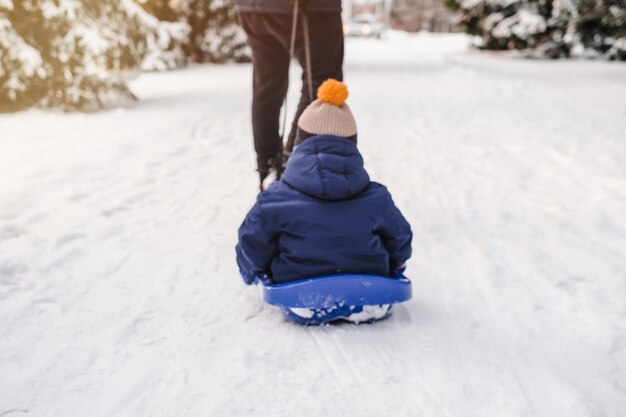 Sfondio sfocato con il padre che porta suo figlio su una slitta attraverso la neve nel parco