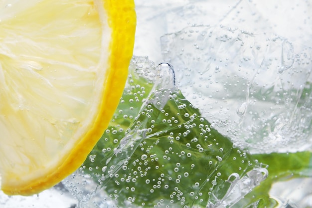 Sfondo astratto di acqua con limoni foglie di menta e cubetti di ghiaccio in vetro fuoco selettivo