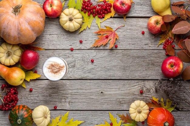 Sfondo autunnale con foglie di acero gialle, mele rosse, zucche e latte piccante. Cornice del raccolto autunnale su legno invecchiato.