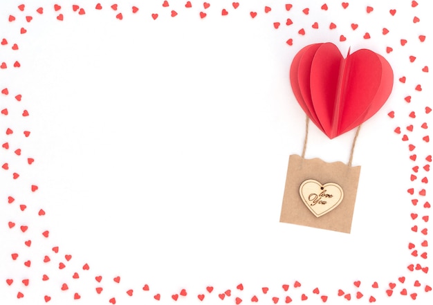 Sfondo bianco di San Valentino con palloncino cuore rosso con cesto con cuore in legno su di esso e tanti cuori rossi. Biglietto di auguri di San Valentino. Stile piatto laici con spazio di copia. Concetto di amore e felicità.