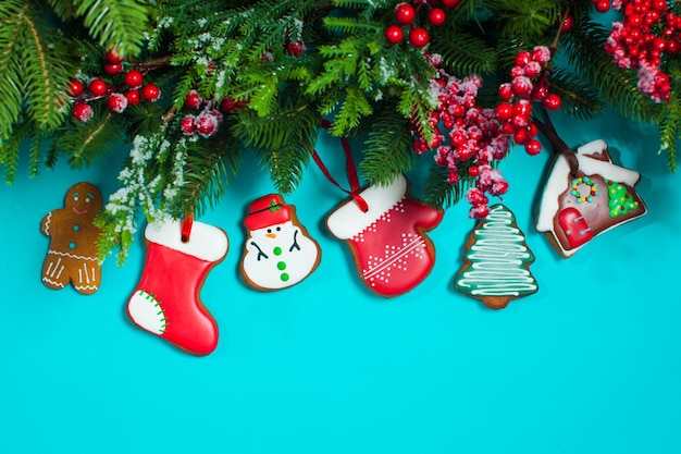 Sfondo blu di Natale con ramo di agrifoglio, bacche, abete e biscotti allo zenzero. Posto per i saluti