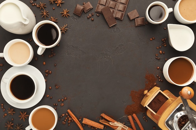 Sfondo caffè con tazze assortite, macinino vintage, fagioli, spezie e cioccolato su ardesia nera, vista dall'alto, spazio copia. Design orizzontale per pubblicità di bar o caffetteria