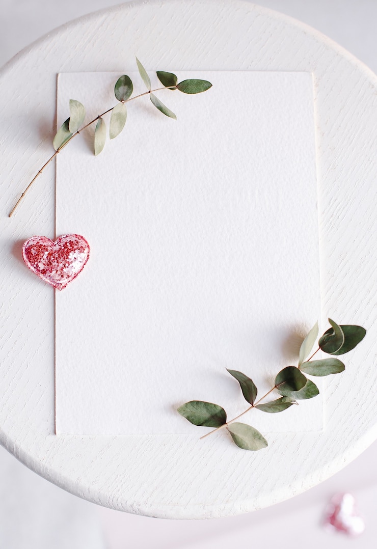 Foto sfondo con copia spazio vuoto sul tavolo bianco con cuore glitterato, ramo di eucalipto, fiori e foglie. carta bianca vista dall'alto, piatto, stile minimal. mock up carta.