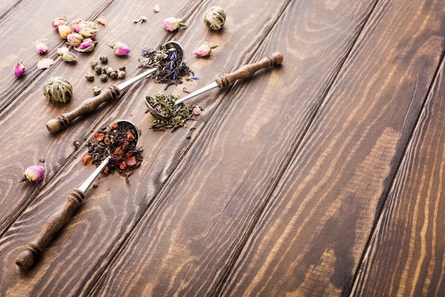 Sfondo con diversi tipi di foglie di tè, nero, verde e fragola sul tavolo di legno.