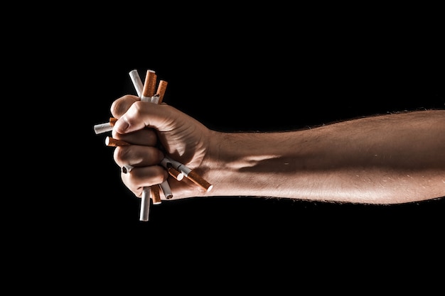 Sfondo creativo, la mano maschile stringe un pugno di una sigaretta.