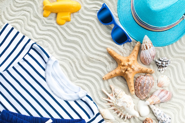 Sfondo del mare. Conchiglie piatte ancora con sabbia bianca e vestiti per bambini su di esso