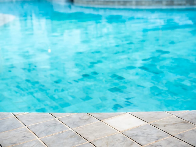 Sfondo della piscina estiva Spazio vuoto sul bordo della piscina piastrelle in pietra di marmo e piscina sfocata sullo sfondo estivo del resort tropicale per la visualizzazione o il montaggio dei tuoi prodotti