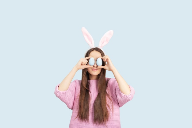 Sfondo delle uova di Pasqua Sconti per le vacanze e concetto di vendita Ragazza felice nelle orecchie del coniglietto con uova decorate sorridenti isolate su uno sfondo blu in studio