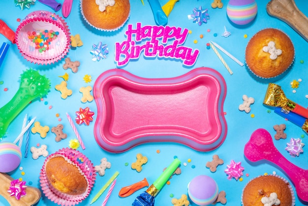 Sfondo di buon compleanno per animali domestici con set di diversi cani snack e giocattoli ciotola per cani a forma di osso cupcakes di compleanno con candele di buon compleanno e accessori Flatlay su sfondo blu vista dall'alto