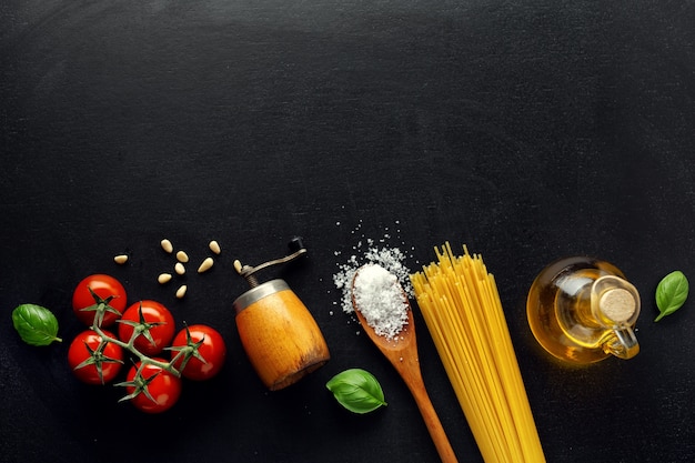 Sfondo di cibo italiano tradizionale con spaghetti pomodori formaggio olive e olio su sfondo scuro.