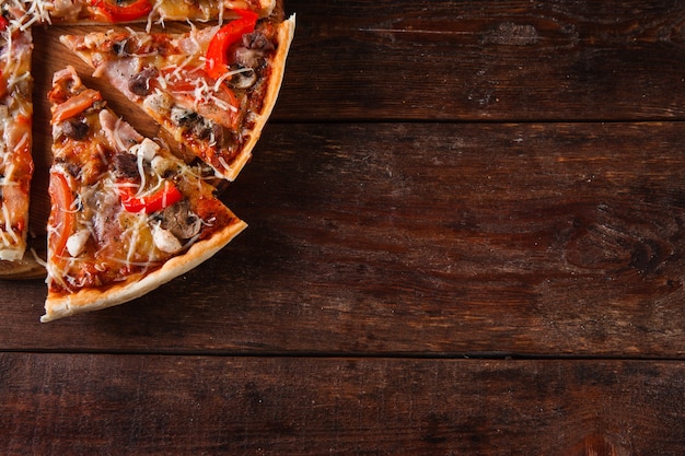 Sfondo di cibo tradizionale italiano. Fette di pizza appetitosa sulla tavola di legno rustica, disposizione piana. Sfondo scuro con spazio libero per il testo.