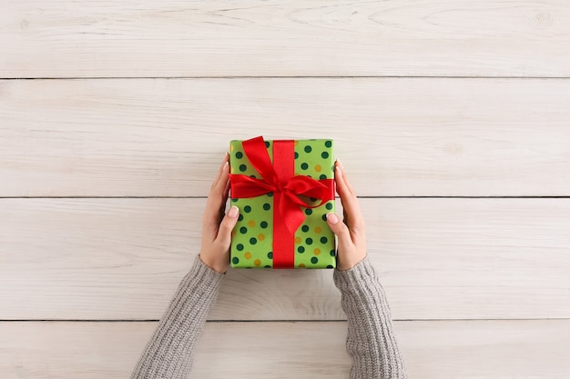 Sfondo di confezioni regalo. Mani femminili che tengono la scatola presente fatta a mano in carta punteggiata verde contro il fondo della tavola in legno bianco. Concetto di preparazione di compleanno o natale, vista dall'alto, spazio di copia