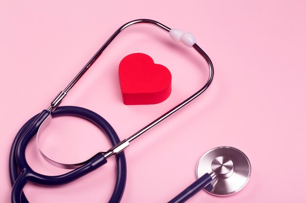 Sfondo di giornata mondiale del cuore. Cuore come simbolo di salute, cura, carità, donazione e cardiologia su uno sfondo rosa con uno statoscopio medico.