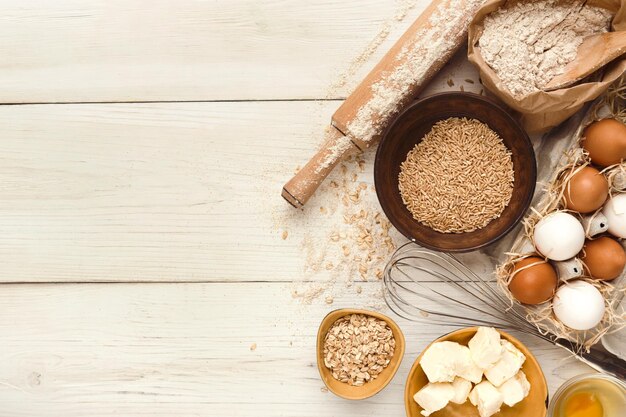 Sfondo di ingredienti da cucina. Bordo di farina, uova, uvetta, zucchero, latte, burro e utensili da cucina su legno rustico bianco con spazio per la copia. Preparazione dell'impasto e concetto di pasticceria, vista dall'alto