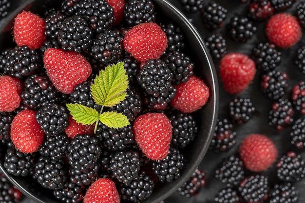 Sfondo di more e lamponi organici freschi da vicino Sacco di frutti di bosco succosi maturi frutti di bosco crudi in un piatto nero Vista dall'alto mora e lampone