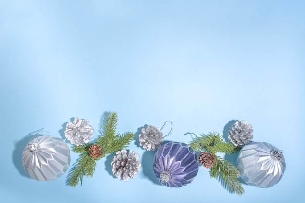 Sfondo di Natale Capodanno. Biglietto di auguri, modello di invito con palline di albero di Natale blu e argento, coni di albero di Natale su sfondo azzurro, spazio di copia flatlay vista dall'alto