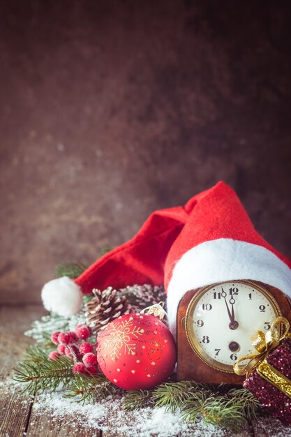 Sfondo di Natale con palle di Natale, orologio, regalo, cappello di Babbo Natale e neve su uno sfondo di legno