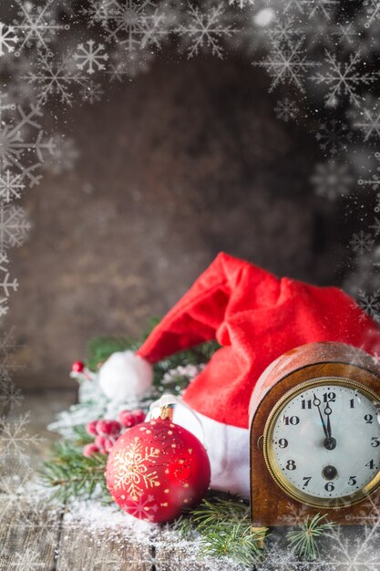 Sfondo di Natale con palle di Natale, orologio, regalo, cappello di Babbo Natale e neve su uno sfondo di legno