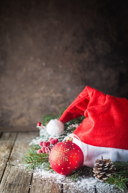 Sfondo di Natale con palle di Natale, regalo, cappello di Babbo Natale e neve su uno sfondo di legno