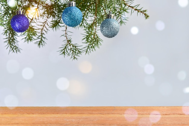 Sfondo di Natale con piano del tavolo in legno, ramo di abete, palline e luci bokeh.