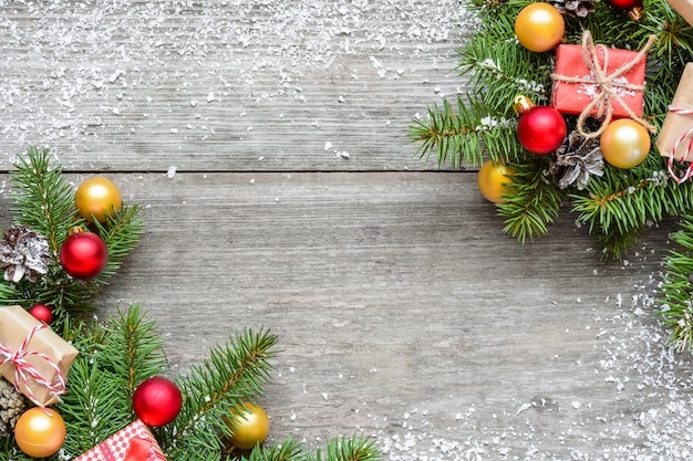 Sfondo di Natale con rami di abete, decorazioni, scatole regalo e pigne su tavola in legno rustico ricoperta di neve. Sfondo di Natale. Disposizione piatta. vista dall'alto con copia spazio