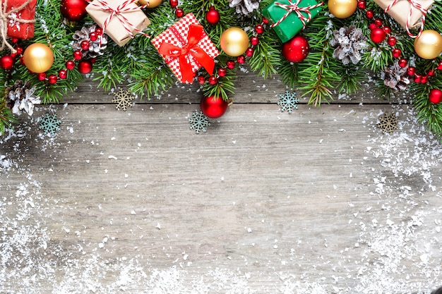 Sfondo di Natale con rami di abete, palline rosse e dorate, scatole regalo e pigne su tavola in legno rustico ricoperta di neve. Disposizione piatta. vista dall'alto con copia spazio